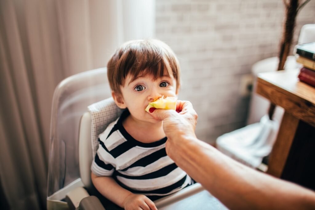 boy in black and white stripe shirt eating yellow fruit sitting on white sofa, Nutrition in Children