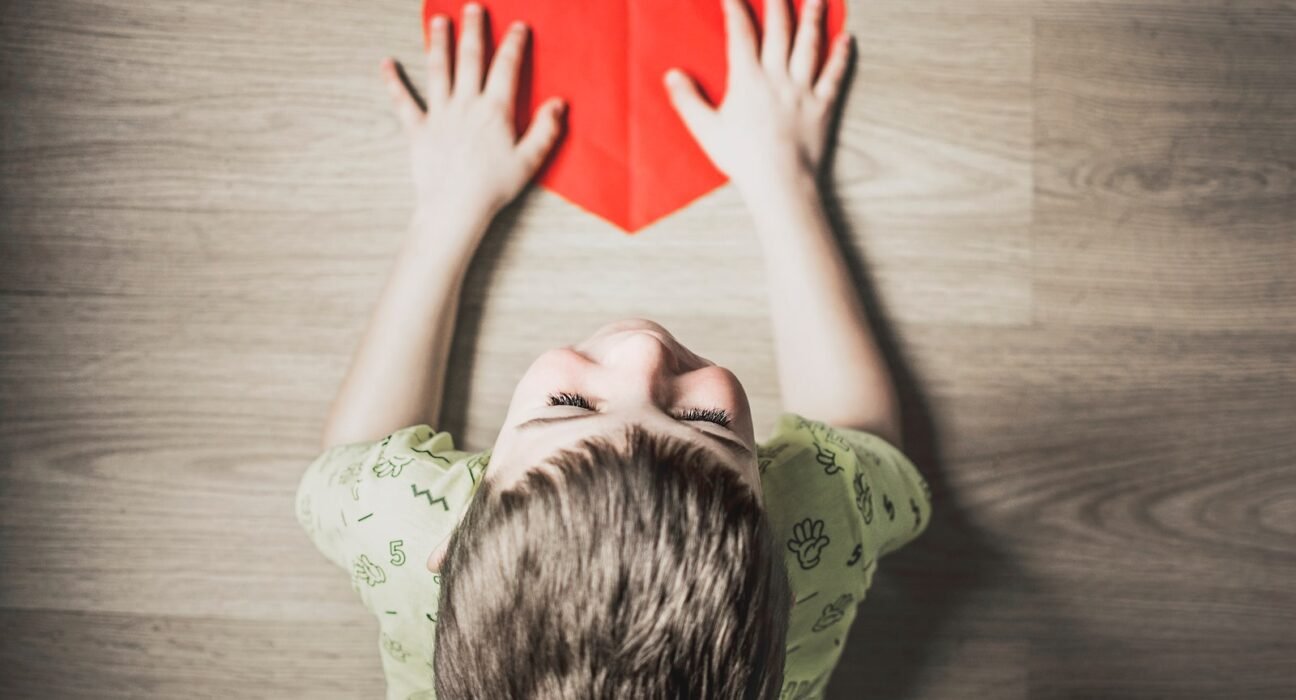 boy in green shirt holding red paper heart cutout on brown table, orthopedics