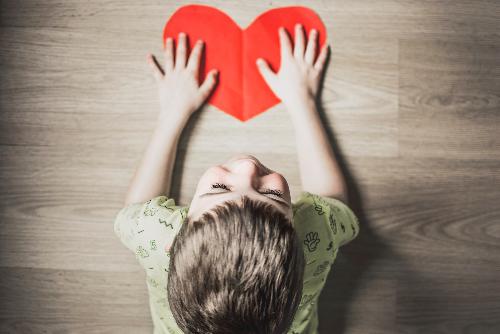 boy in green shirt holding red paper heart cutout on brown table, orthopedics