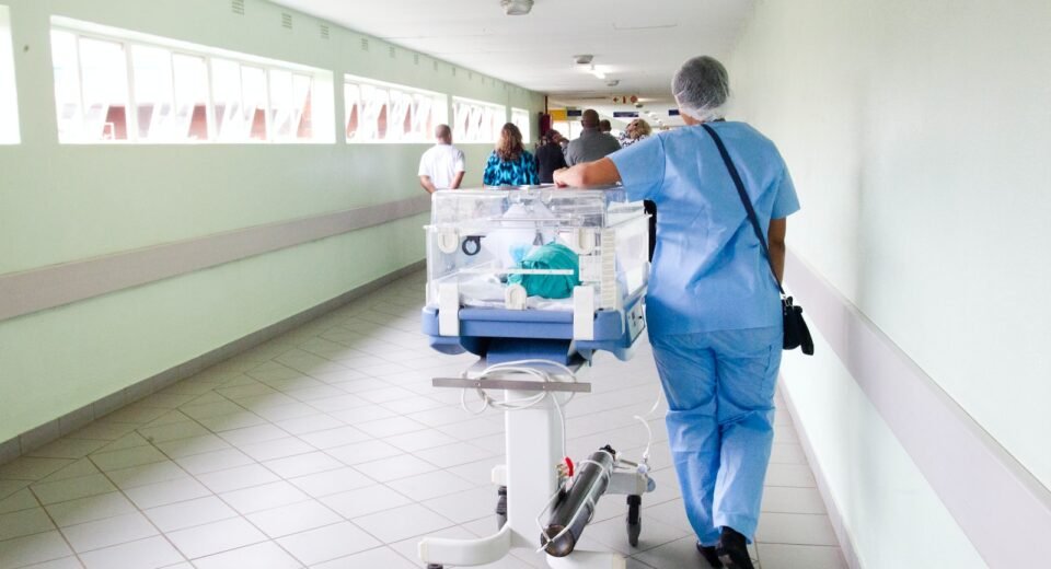 person walking on hallway in blue scrub suit near incubator